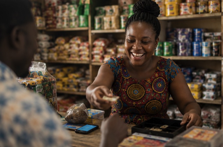 A trader handing change across her provisions-store counter